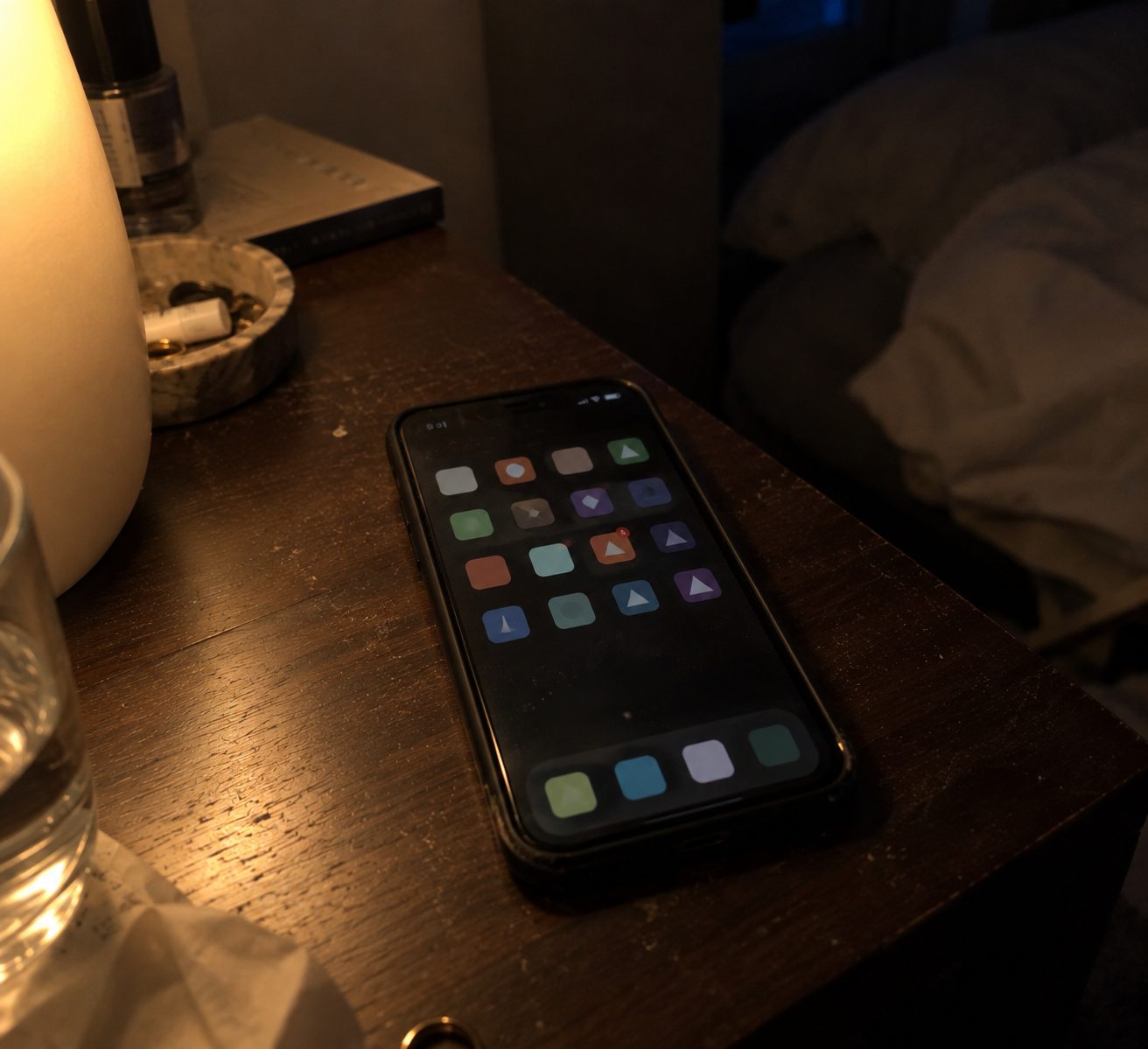 Un smartphone posé sur une table de nuit, écran d'accueil allumé, dans une chambre sombre le soir